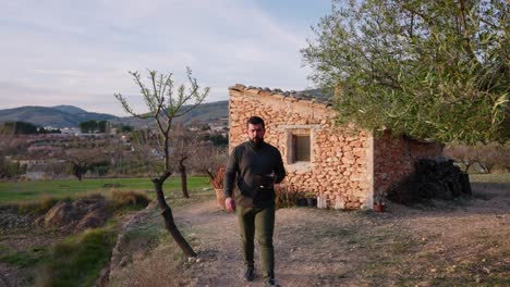 man walks among almond blossom trees at sunset, with an old mediterranean-style stone hut in early spring