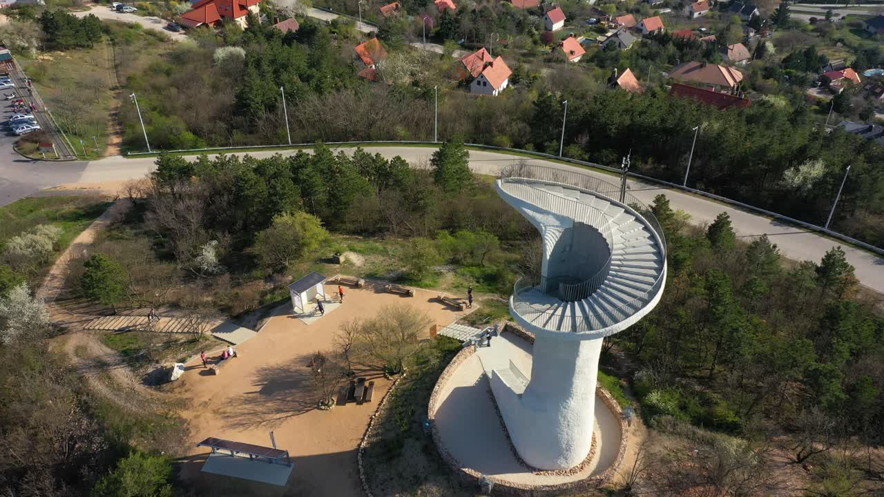 Aerial View of a Modern Spiral Observation Tower on a Hilltop overlooking a Village and Lake