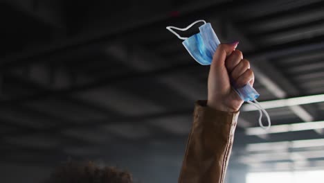 Part-of-african-american-woman-hand-protesting-while-holding-face-mask-in-empty-parking-garage