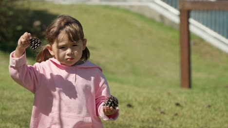 una niña linda cuidando estroboscopios de pino o conos en ambas manos y caminando por el césped en cámara lenta