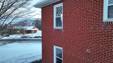 aerial push-in on rear bedroom window of two story brick home covered in winter snow