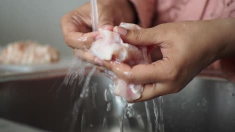 woman washing raw chicken breast in kitchen sink