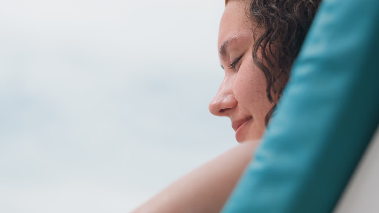 Calm woman relaxing. Peaceful woman reclines by tranquil sea. Serene female rests peacefully near quiet ocean shore. Relaxed woman with golden headpiece enjoys calmness beside peaceful seaside