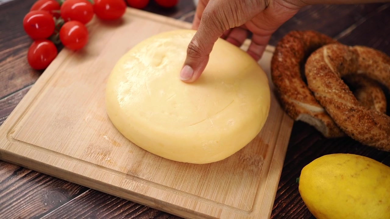 Mano che preme e solleva un formaggio giallo rotondo su un tagliere di legno