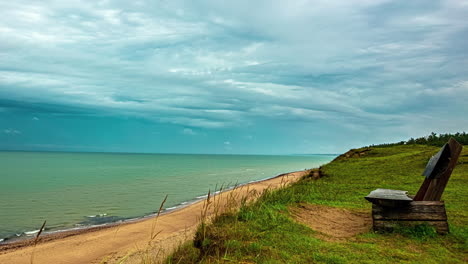 lonely wooden bench near calm ocean against rolling cloudscape