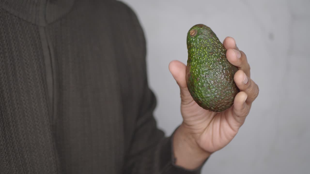Primo piano di una mano che tiene e ruota un avocado fresco.