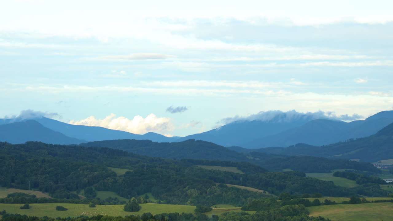 화창한 날 낮은 구름이 언덕 위로 이동하는 동안 언덕으로 가득 찬 산악 풍경 위로 움직이는 흰 구름