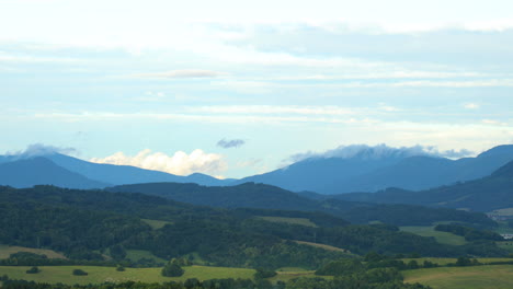 Weiße-Wolken-Ziehen-An-Einem-Sonnigen-Tag-über-Eine-Bergige-Landschaft-Voller-Hügel.-Niedrige-Wolken-Ziehen-über-Die-Hügel