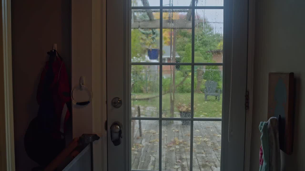 A man quickly and efficiently washes a home patio door window with a long handle brush and hose