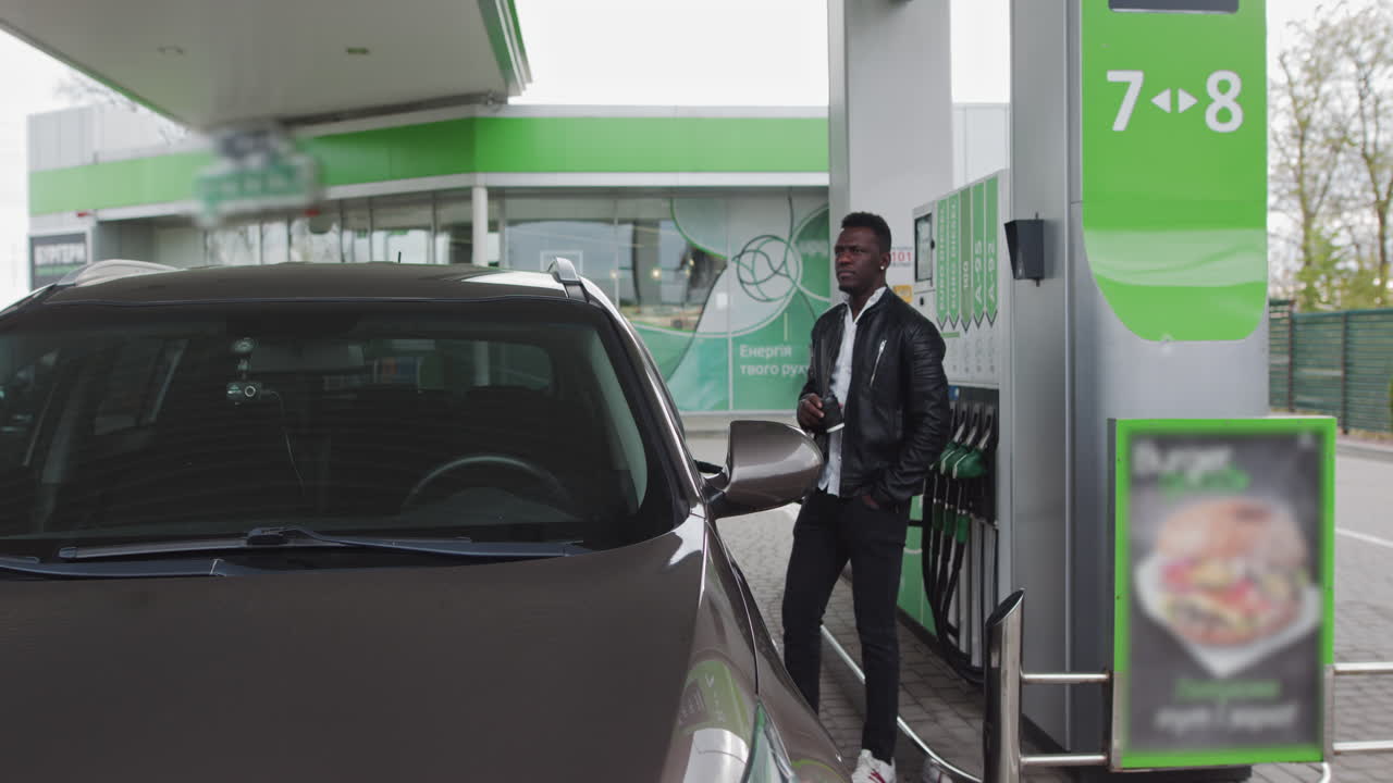 Rifornimento auto durante il viaggio: uomo afroamericano si ferma al distributore di benzina e beve un caffè