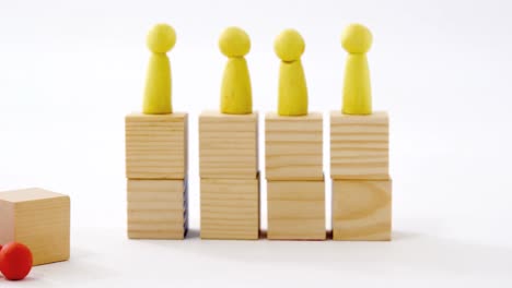 yellow figurines on wooden blocks in a row and red figurine fallen on ground