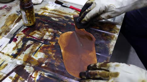 man painting leather with slow movements using gloves on the table full of objects