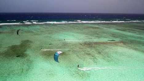 Kitesurfer-Gleiten-über-Klares,-Türkisfarbenes-Wasser-An-Einem-Barriereriff-Vorbei,-Lebendige-Und-Aktive-Szene,-Sonniger-Tag,-Luftaufnahme