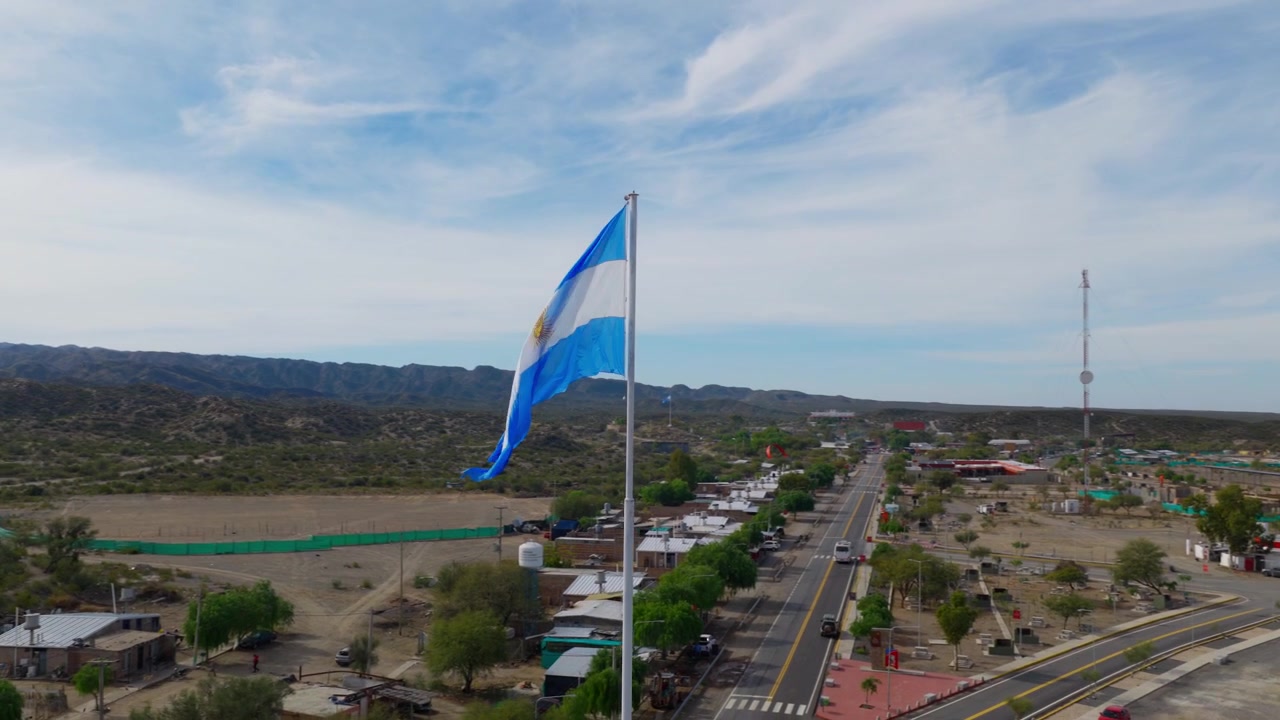 Ampia ripresa orbitale con drone attorno a una grande bandiera dell'Argentina sull'asta in città.