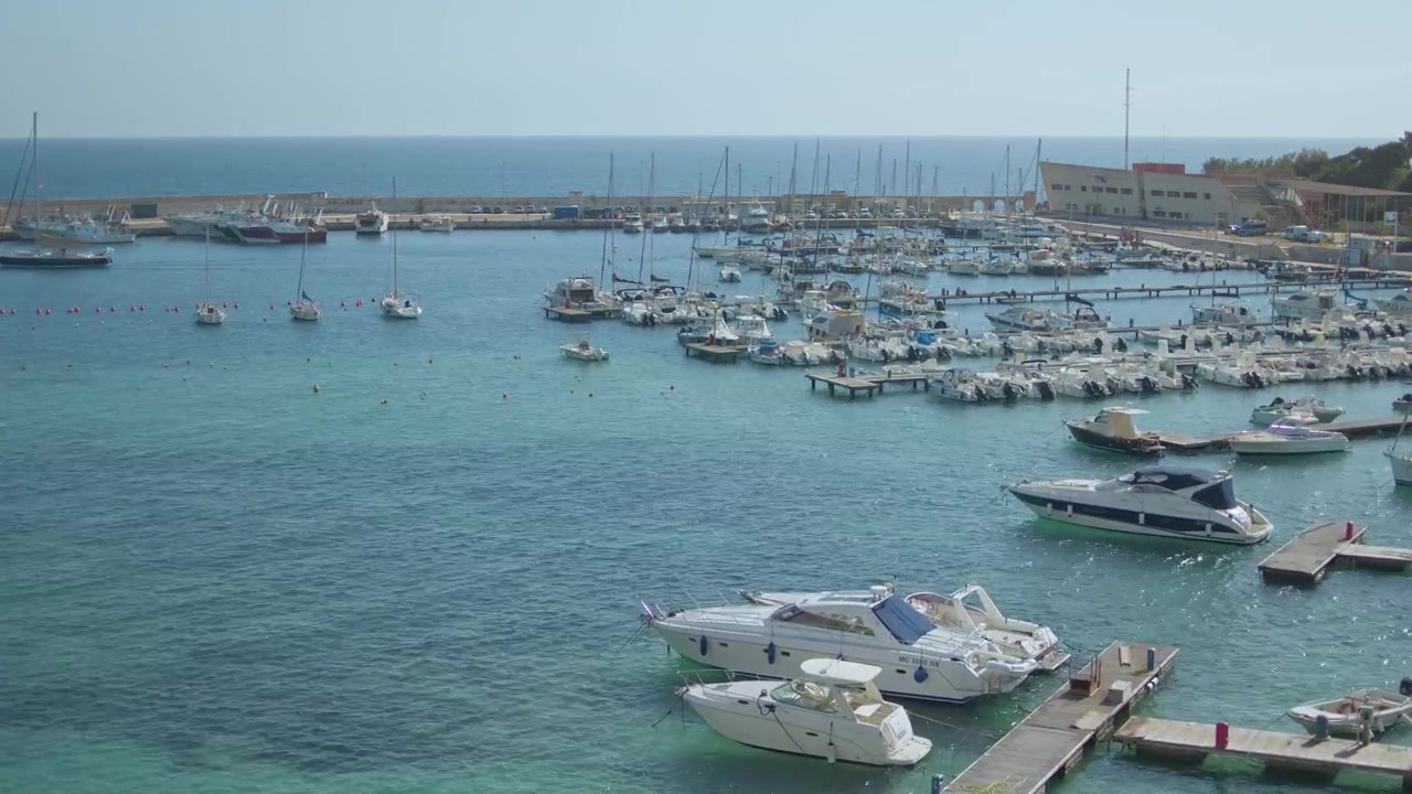 La marina di Otranto ospita yacht e imbarcazioni da diporto lungo la costa adriatica della Puglia, Italia, con vista su acque turchesi e un vivace ambiente portuale, ripresa in timelapse con vista elevata