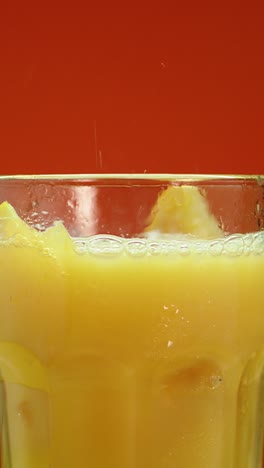 fresh orange juice pouring into glass with ice and orange slices in vertical close-up