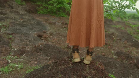 woman in brown dress and boots standing on a hill