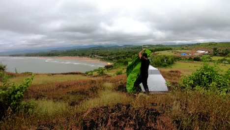 man-pitching-his-camping-tent-at-mountain-top-with-amazing-view-and-dramatic-sky-at-evening