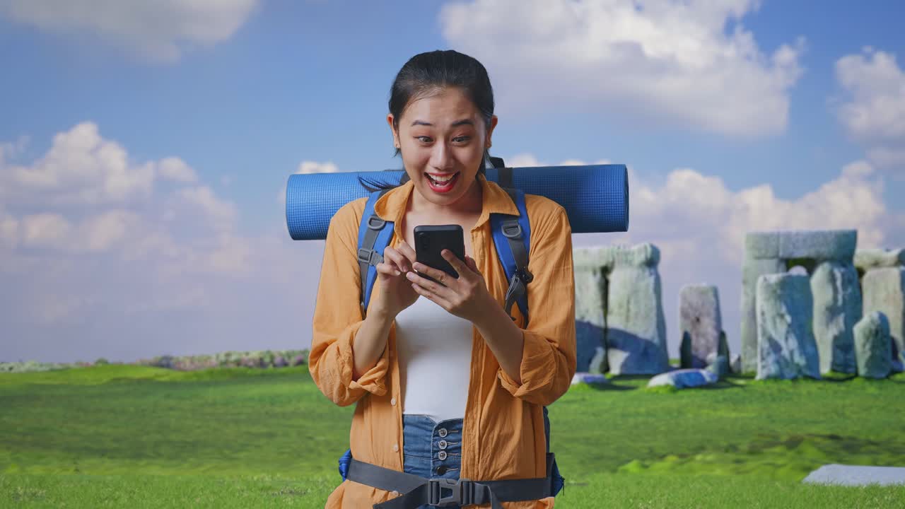 Asian Female Hiker With Mountaineering Backpack Looking At The Smartphone And Saying Wow While Traveling In Stonehenge