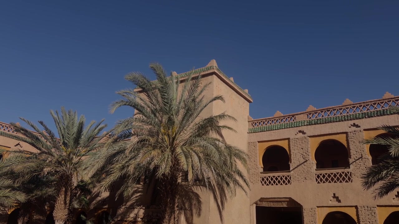 Edificio in stile kasbah marocchina ornato con balconi ad arco e finiture in zellige accanto a alte palme