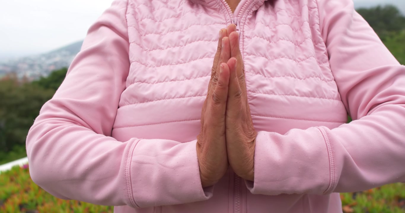 African American senior pressing palms adjusting fingers starting namaste in pink jacket on terrace
