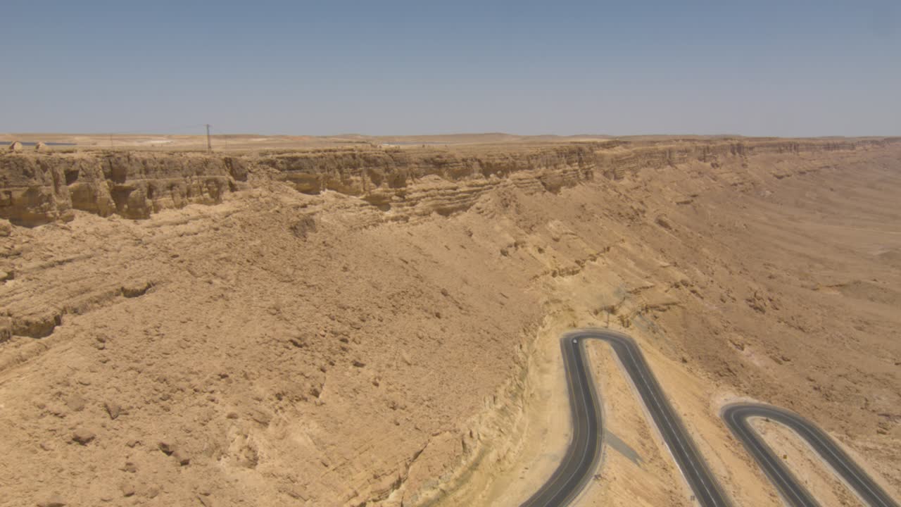 High aerial, rugged steep desert mountain side with car driving on twisty road