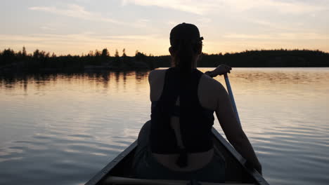 woman paddling a canoe into beautiful sunset reflections in the boundary waters