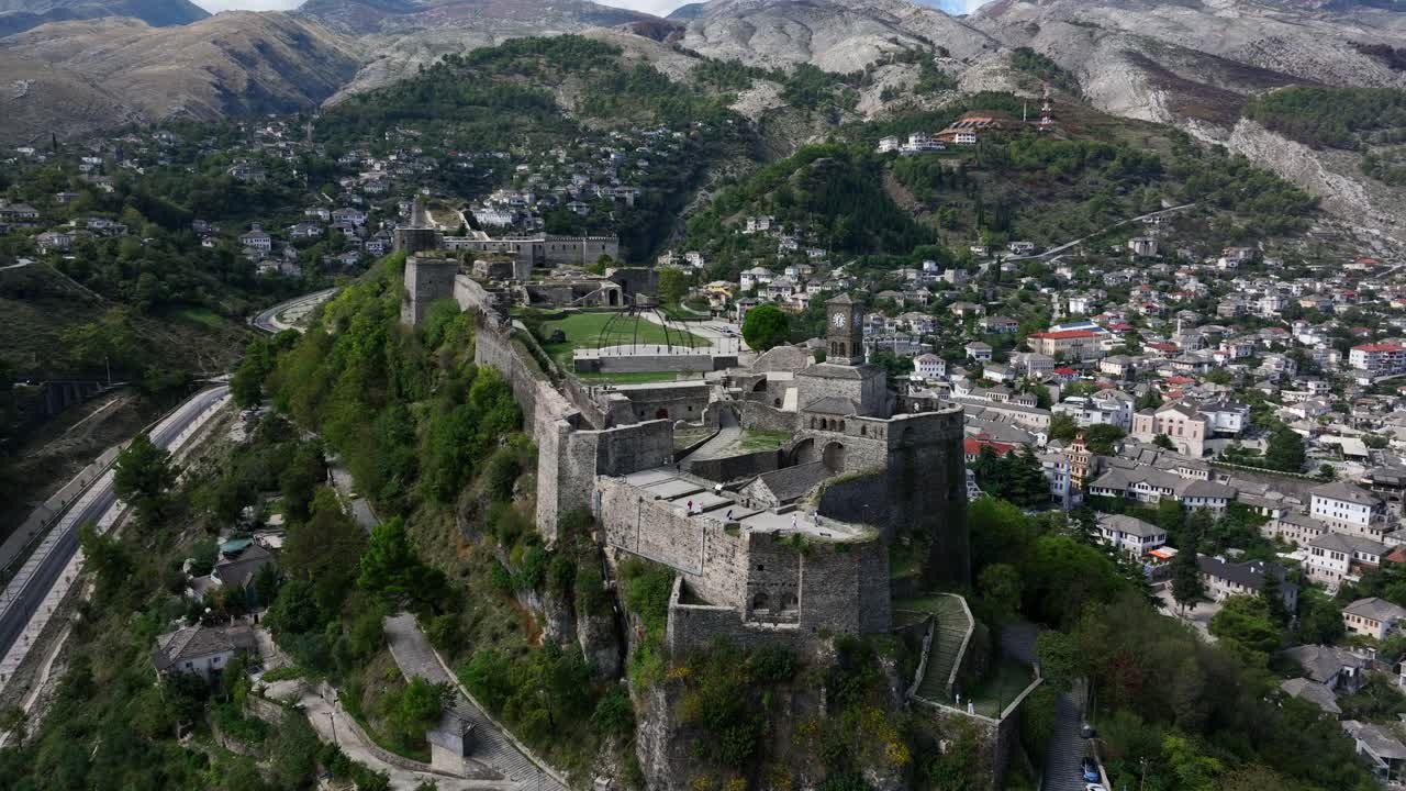 Historic stone fortress above Albanian town, surrounded by green hills and homes