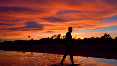 el hombre camina sobre el agua mirando un cielo con nubes en llamas coloreadas por la puesta de sol y la luz del sol.