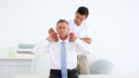 Stressed-businessman-getting-his-shoulders-checked-by-physiotherapist
