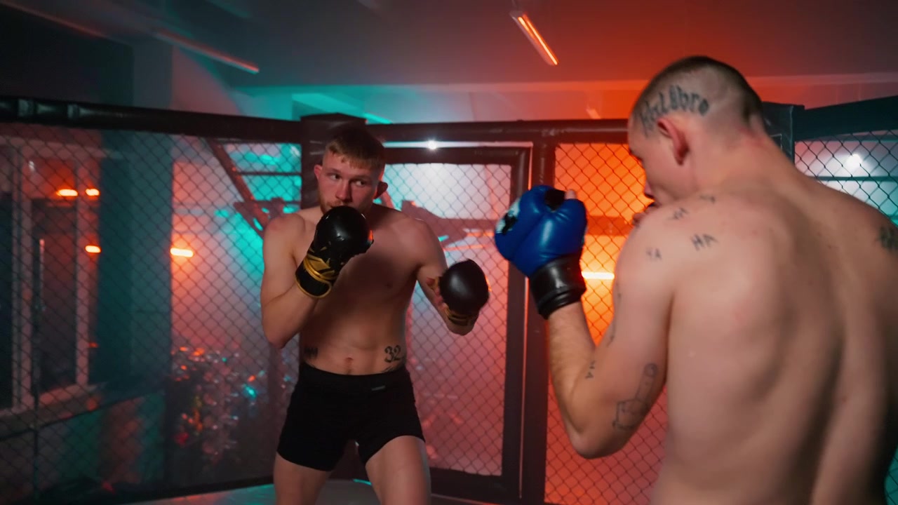 To mandlige kæmpere sparrer i et MMA-bur med dramatisk belysning