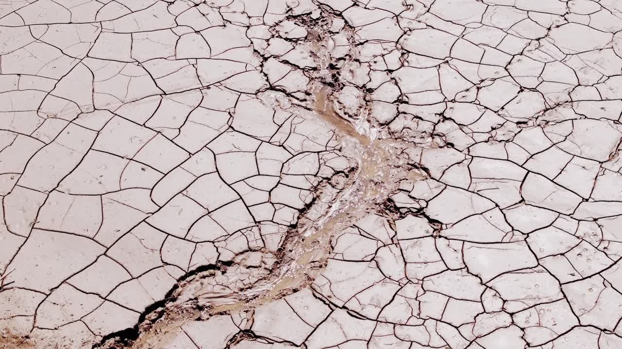 Aerial shot captures dry cracked earth with reflective water in desert valley