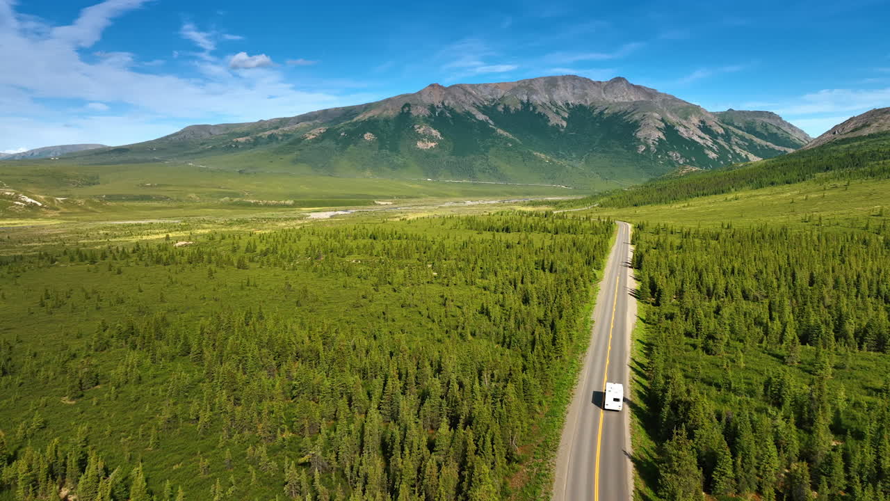 Viaggio sereno sulle strade tortuose dell'Alaska. Esplora i paesaggi mozzafiato dell'Alaska dall'alto, con foreste infinite e maestose montagne sotto un cielo luminoso.