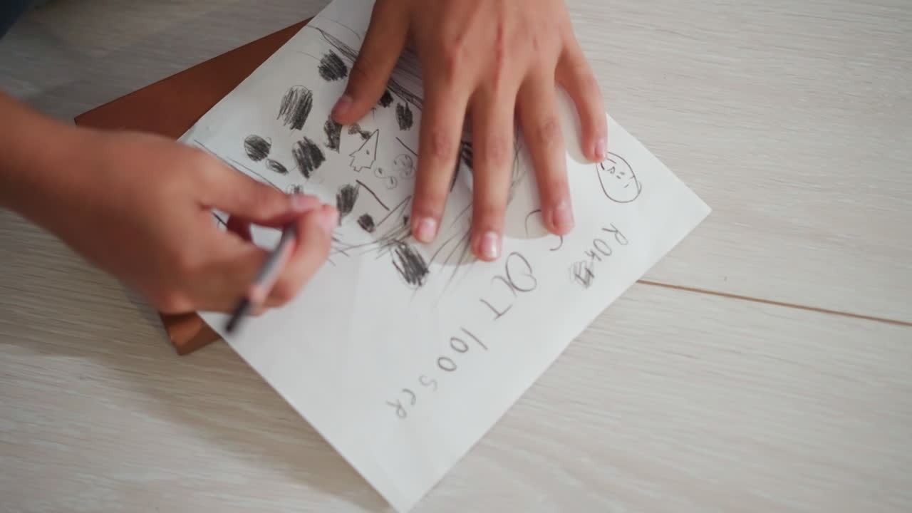 primer plano de la mano de un niño dibujando un gato a lápiz sobre papel blanco mientras está sentado en el suelo de madera, mostrando energía creativa, imaginación infantil y alegría de dibujar con texto escrito a mano