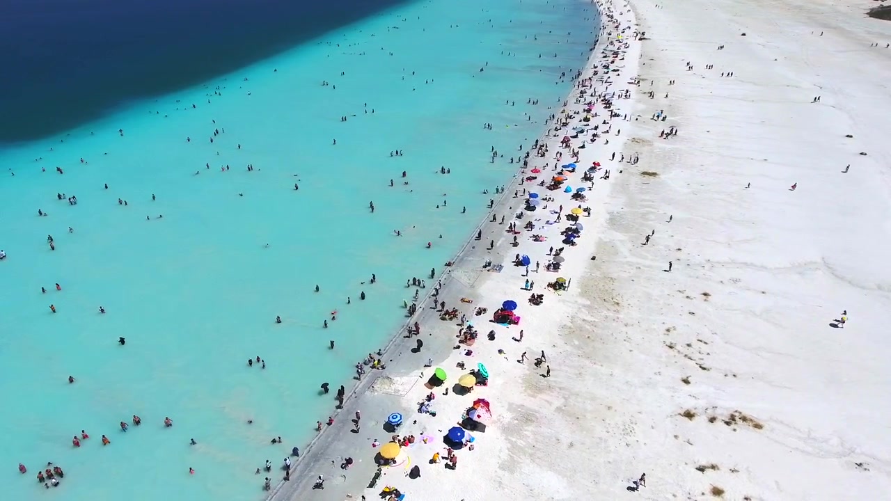 Luftfoto af overfyldt hvid sandstrand med turkisblåt vand