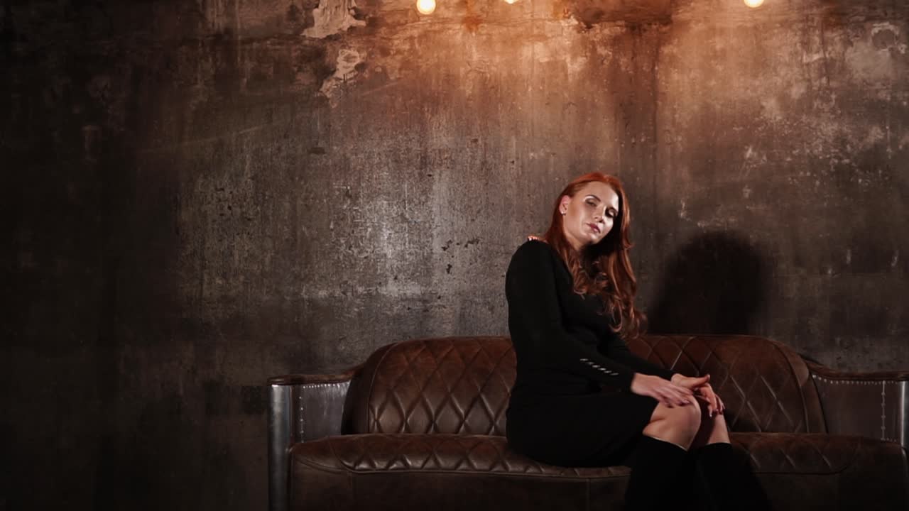 산업 스타일의 스튜디오에서 가죽 소파에 검은 드레스를 입은 여자