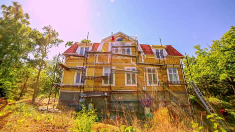 static shot of renovation workers renovating an old wooden cottage in the middle of woods on a bright sunny day in timelapse