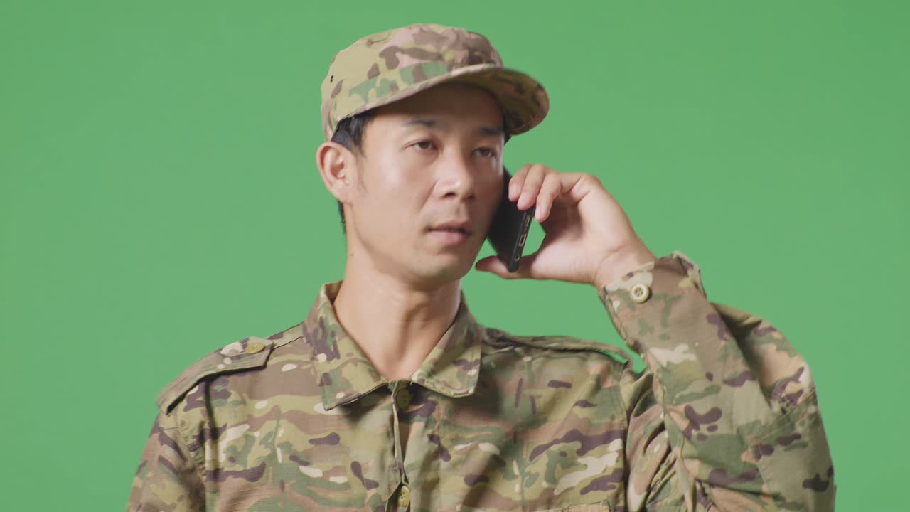 녹색 스크린 배경 스튜디오에서 는 동안 스마트폰으로 이야기하고 주변을 둘러보는 아시아 남자 군인의 클로즈업