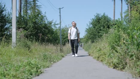 young man walking with guitar on street near forest