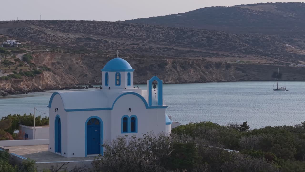 Orbit aerial view of the chapel at Amopi Beach, Karpathos, with the turquoise sea and mountains forming a stunning backdrop