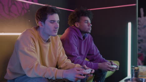 two concentrated friends playing video games sitting on sofa at home