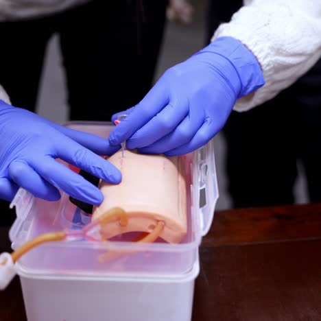 hands in gloves doing injection on a dummy arm. practitioner learning to prick with a syringe into a mannequin hand. close-up