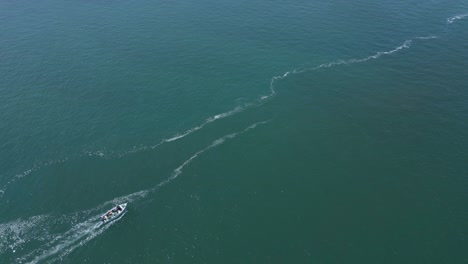 vista aérea de un avión no tripulado rastreando un yate a alta velocidad en una bahía durante un día soleado - capturado en cascais, portugal