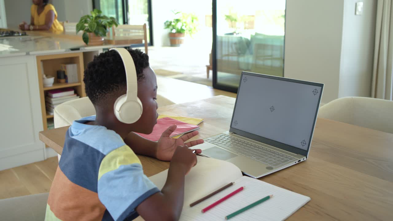 Família afro-americana conversando em casa enquanto a criança participa de uma aula on-line usando um laptop com headset