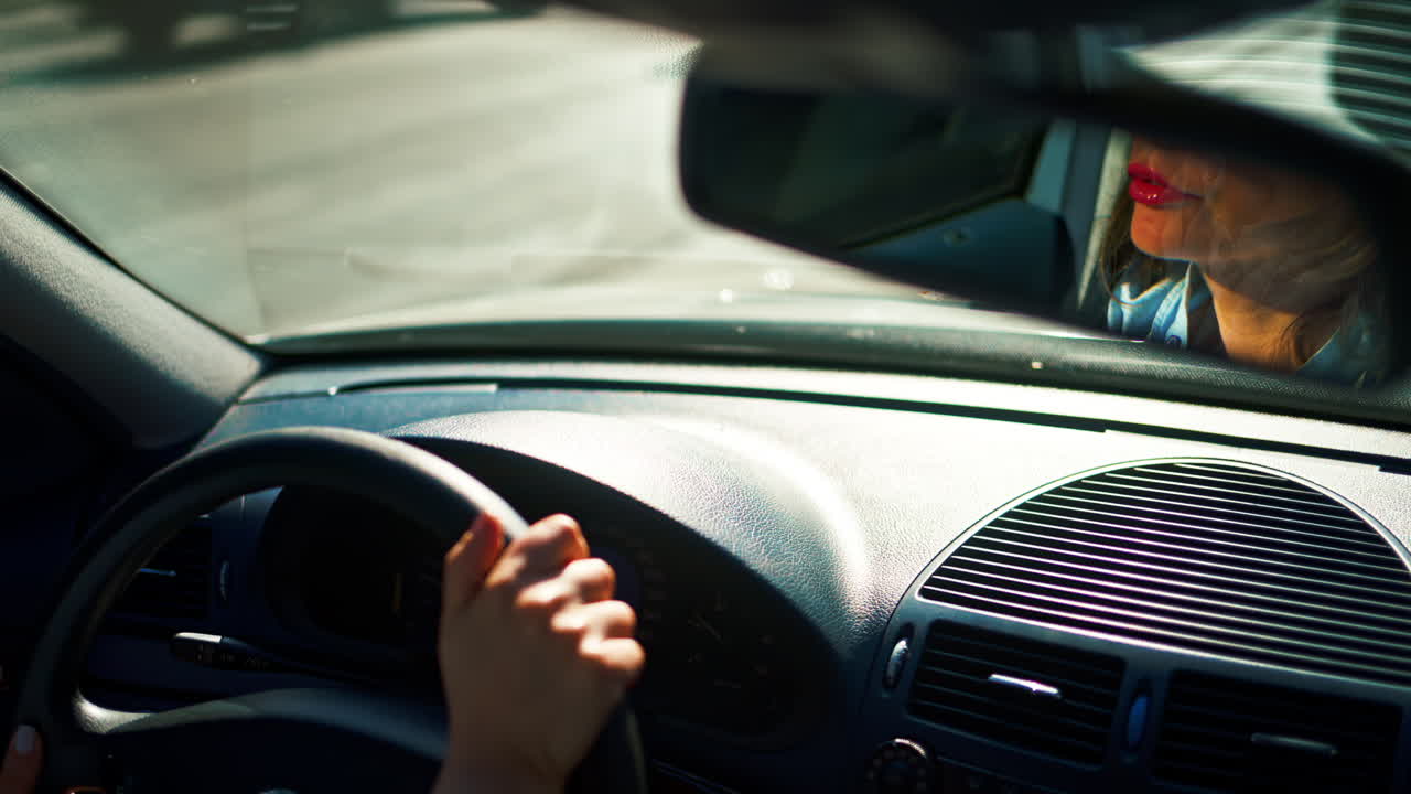 Woman's reflection in the mirror, driving the car in the city traffic, in daylight