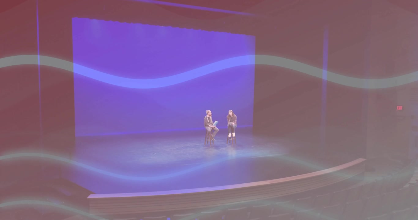 Kvinnelig foredragsholder går inn i teater under blåbelyst bølgelys og engasjerer seg i diskusjon med kollega
