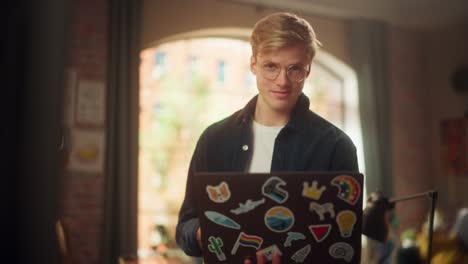 stylish person using laptop computer with diverse lgbtq+ stickers while standing at loft studio. creative young man browsing internet and managing social media. slow motion shot