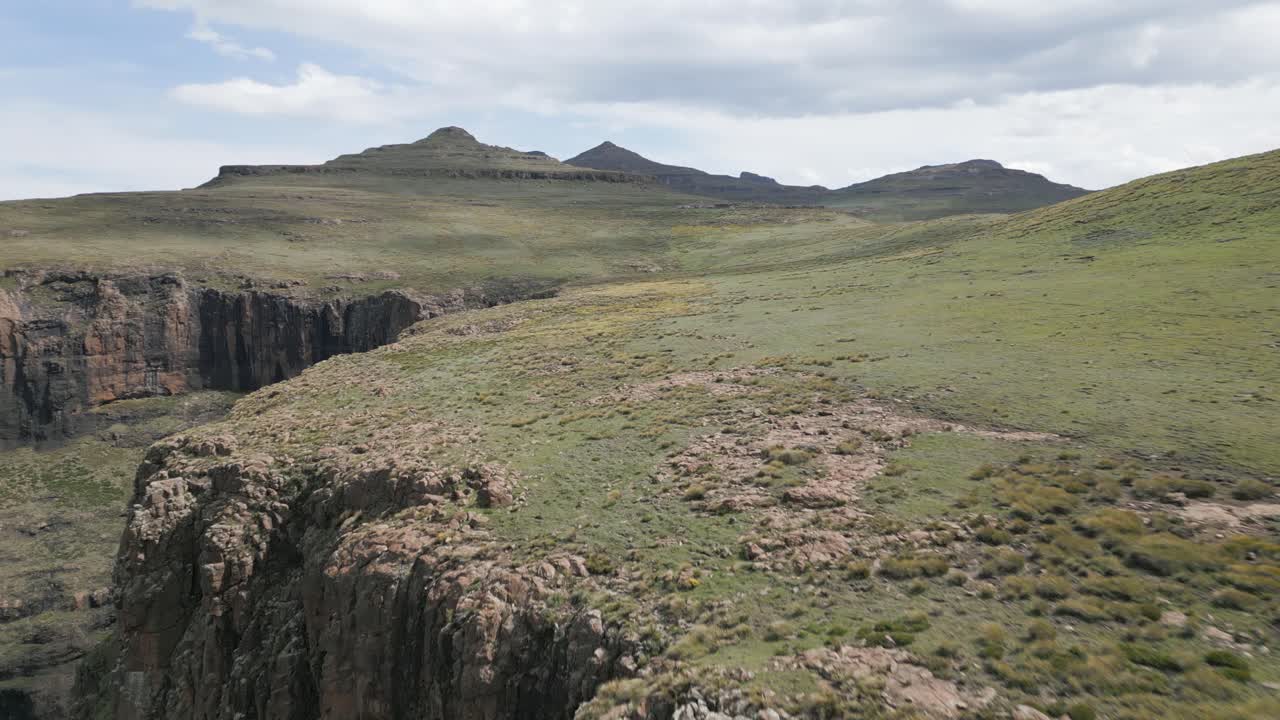 Vertikale Steilklippen am Rande eines grünen Grasland-Bergplateaus.