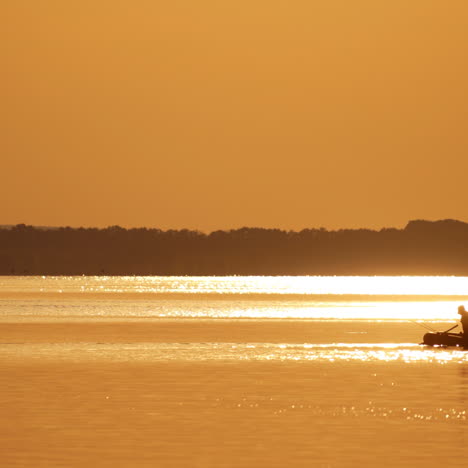 fisherman in a boat at golden sunset time. silhouette of man floating with oars on a small rowboat in the evening. beautiful sunset in the river and man in boat with fishing rods.
