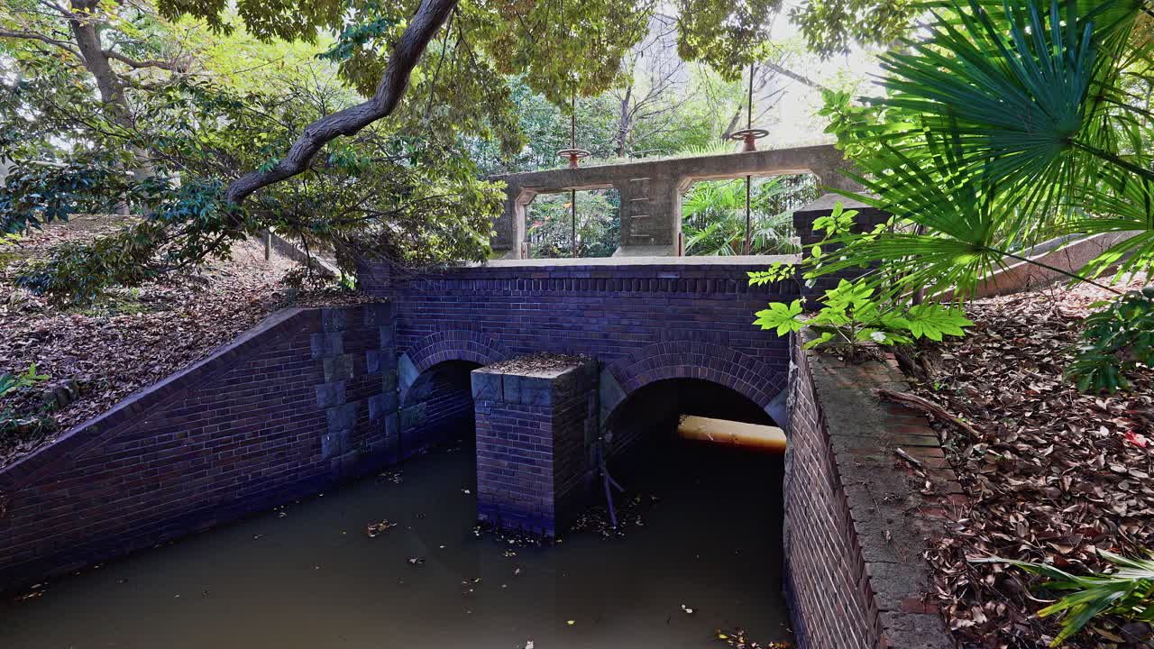The brick archway and channel of the historic Jinzaemon Weir, with the concrete gate structure visible in the background